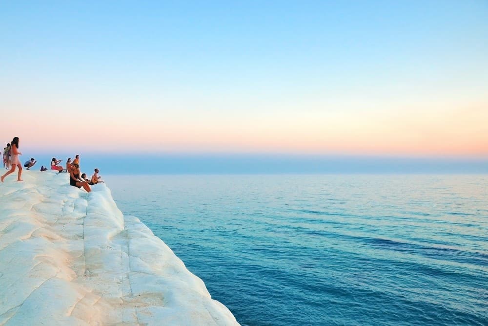 Eine Gruppe von Menschen sitzt während eines All-Inclusive-Urlaubs in Italien auf einer Klippe mit Blick auf das Meer.