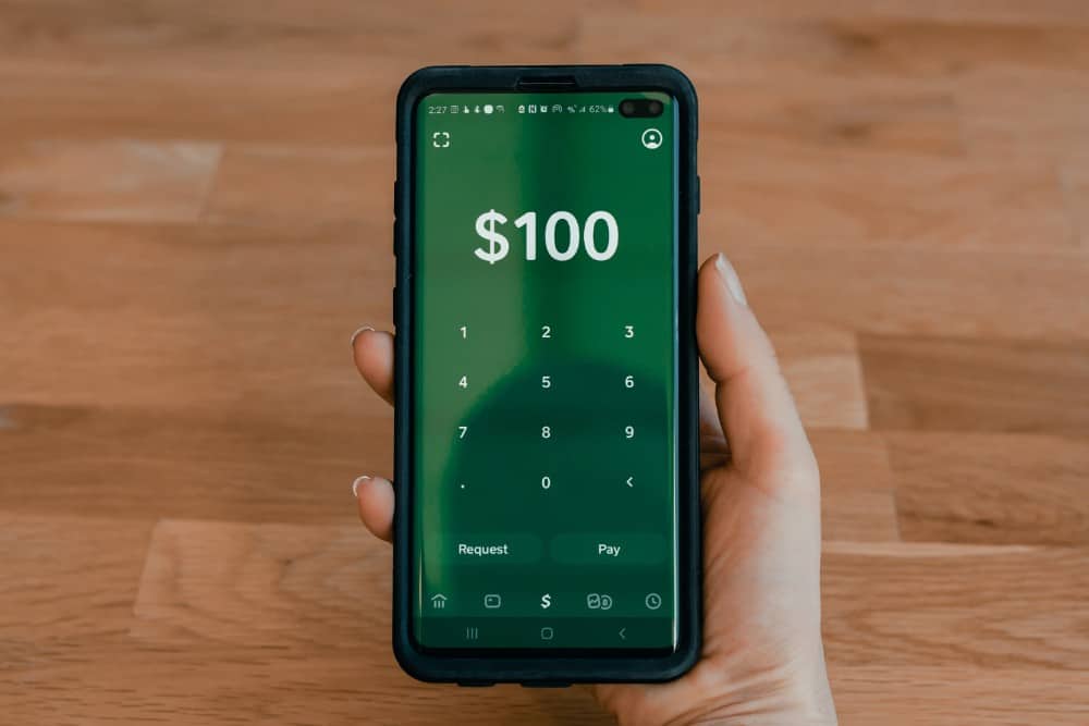 Eine Person nutzt Transferwise, um Geld ins Ausland zu senden, während sie ein Smartphone mit einem 100-Dollar-Schein in der Hand hält.